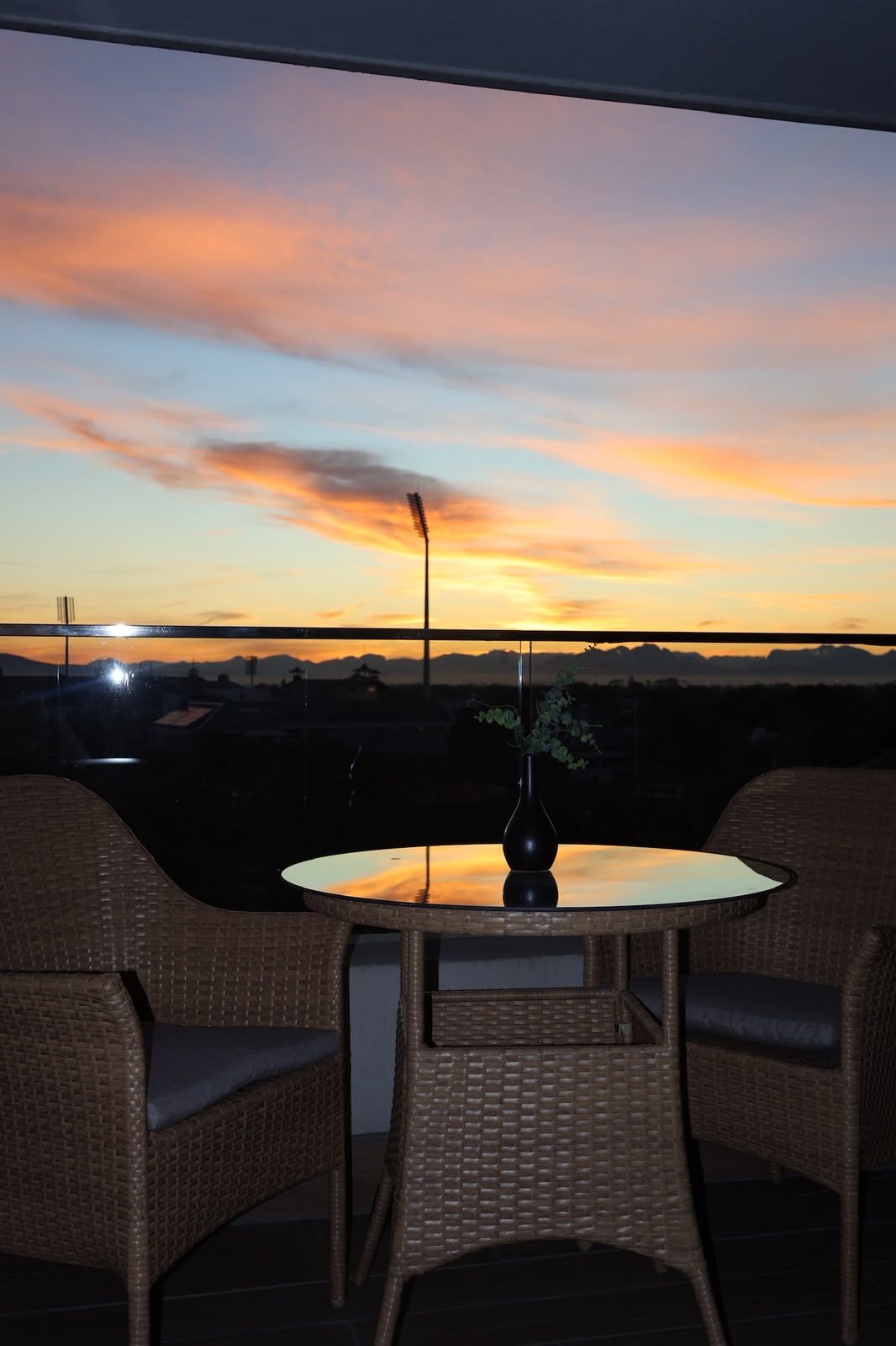Un área de estar al aire libre con mobiliario de mimbre y una mesa, con vista a un atardecer.
