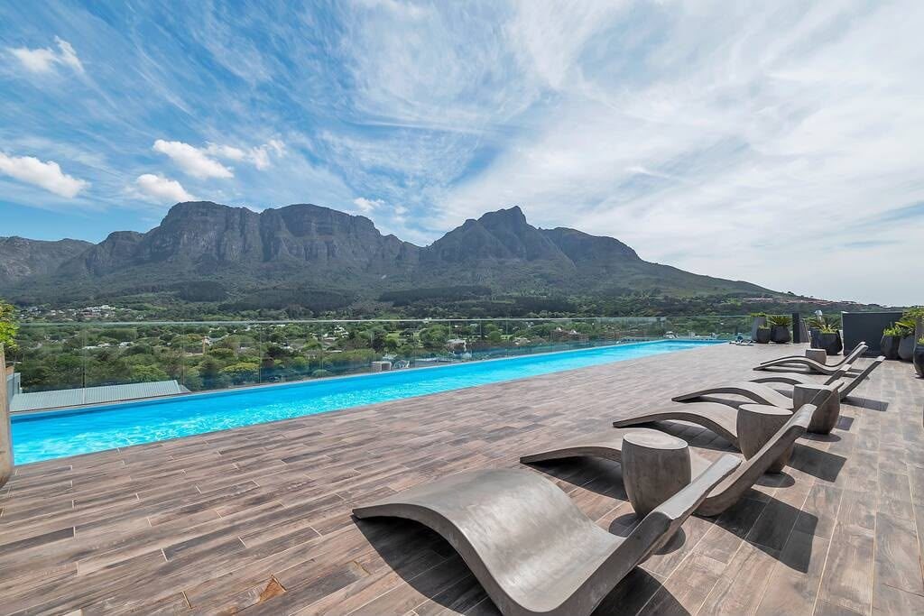 Un área de piscina en la azotea con vistas a montañas, sillas de descanso y una terraza de madera.