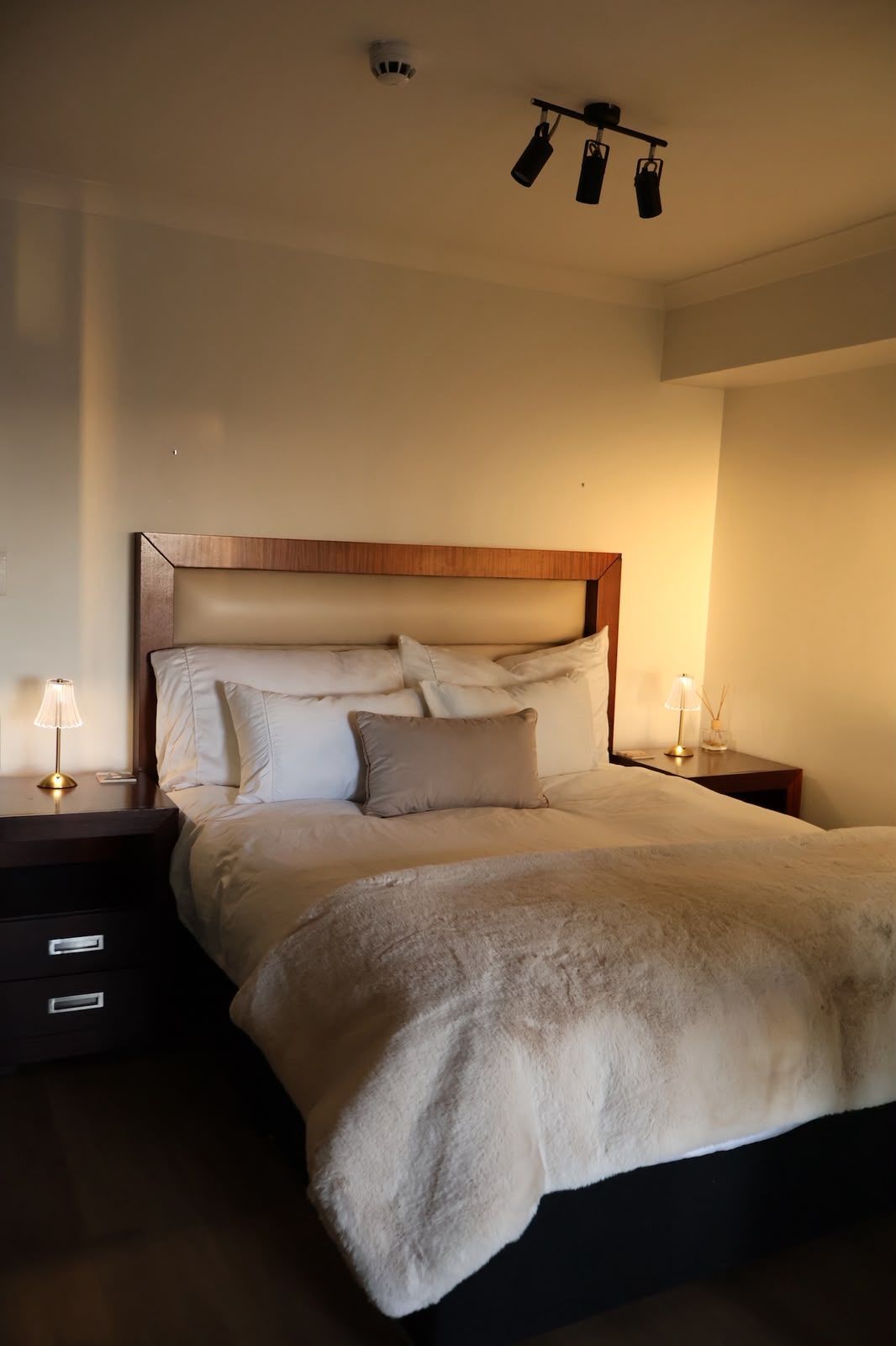 Un dormitorio con una cama grande, dos mesitas de noche y una lámpara en el techo.