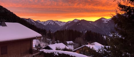 A snow-covered mountain landscape with a wooden cabin and a house in the foreground.