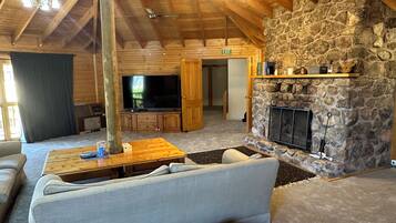 A cozy living room with a stone fireplace, wooden ceiling beams, and a flat-screen TV.
