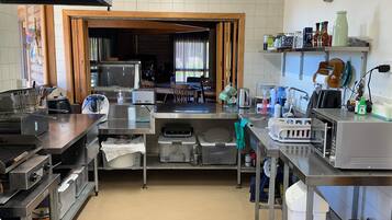 A commercial kitchen with stainless steel appliances, a wooden door leading to a dining area, and various kitchen utensils and supplies on the countertops.