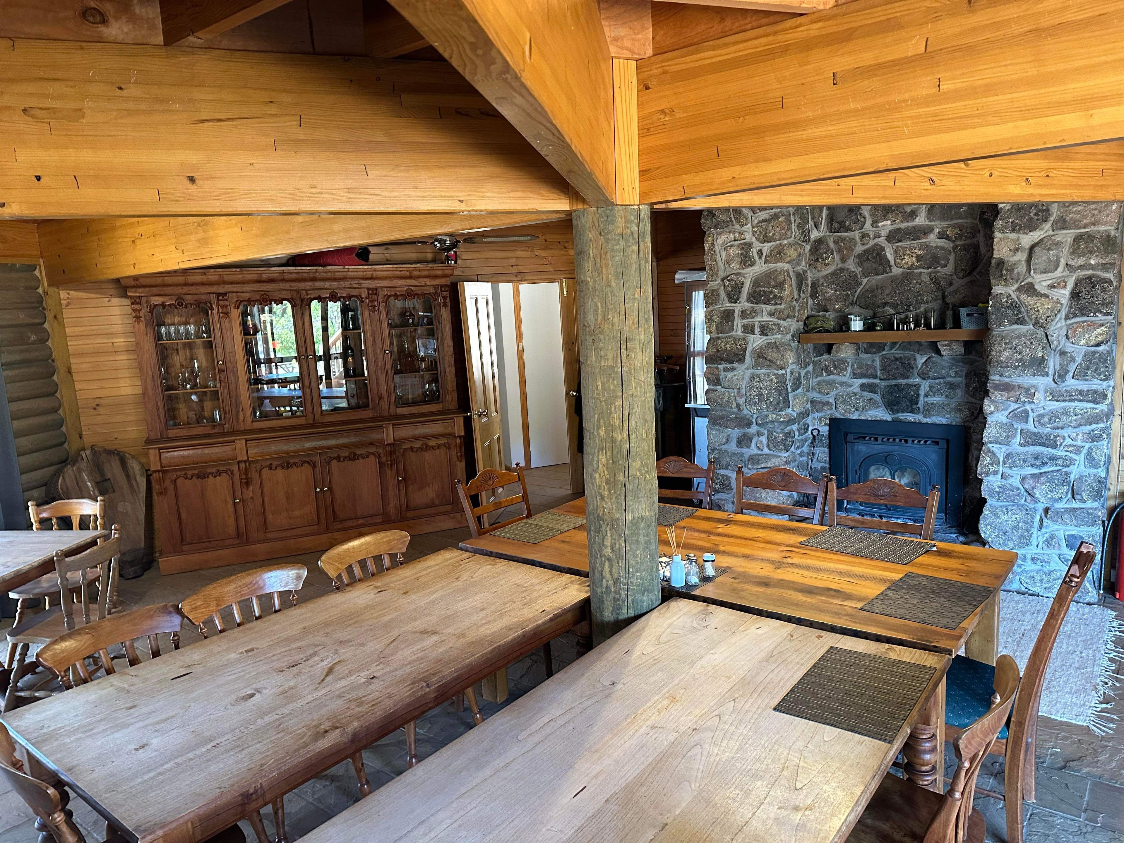 A rustic wooden interior with a stone fireplace, wooden dining table, and chairs.