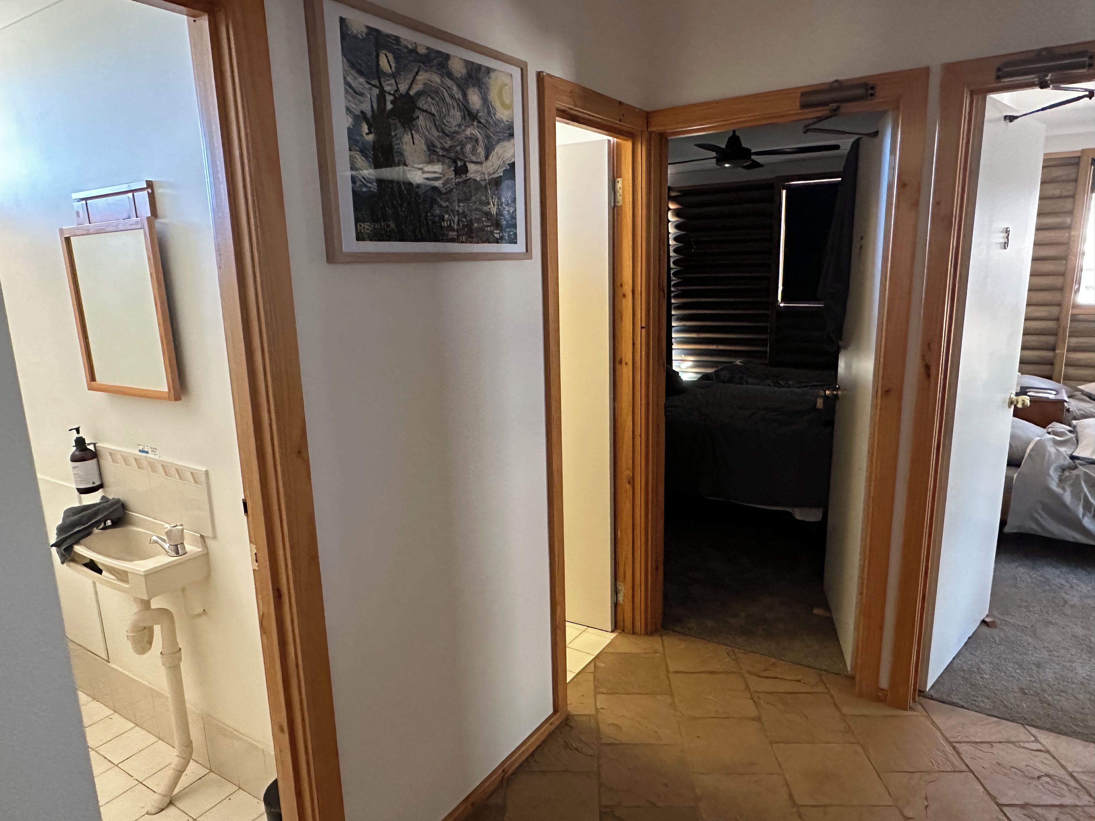 Ein Flur mit einer Holztür, die zu einem Schlafzimmer führt, einem Waschbecken mit Spiegel und einem gerahmten Gemälde an der Wand.