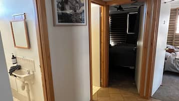Ein Flur mit einer Holztür, die zu einem Schlafzimmer führt, einem Waschbecken mit Spiegel und einem gerahmten Gemälde an der Wand.