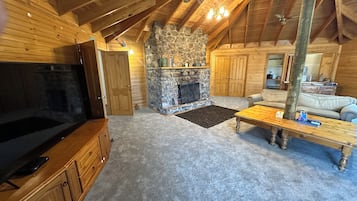 A cozy living room with a stone fireplace, wooden furniture, and a ceiling fan.
