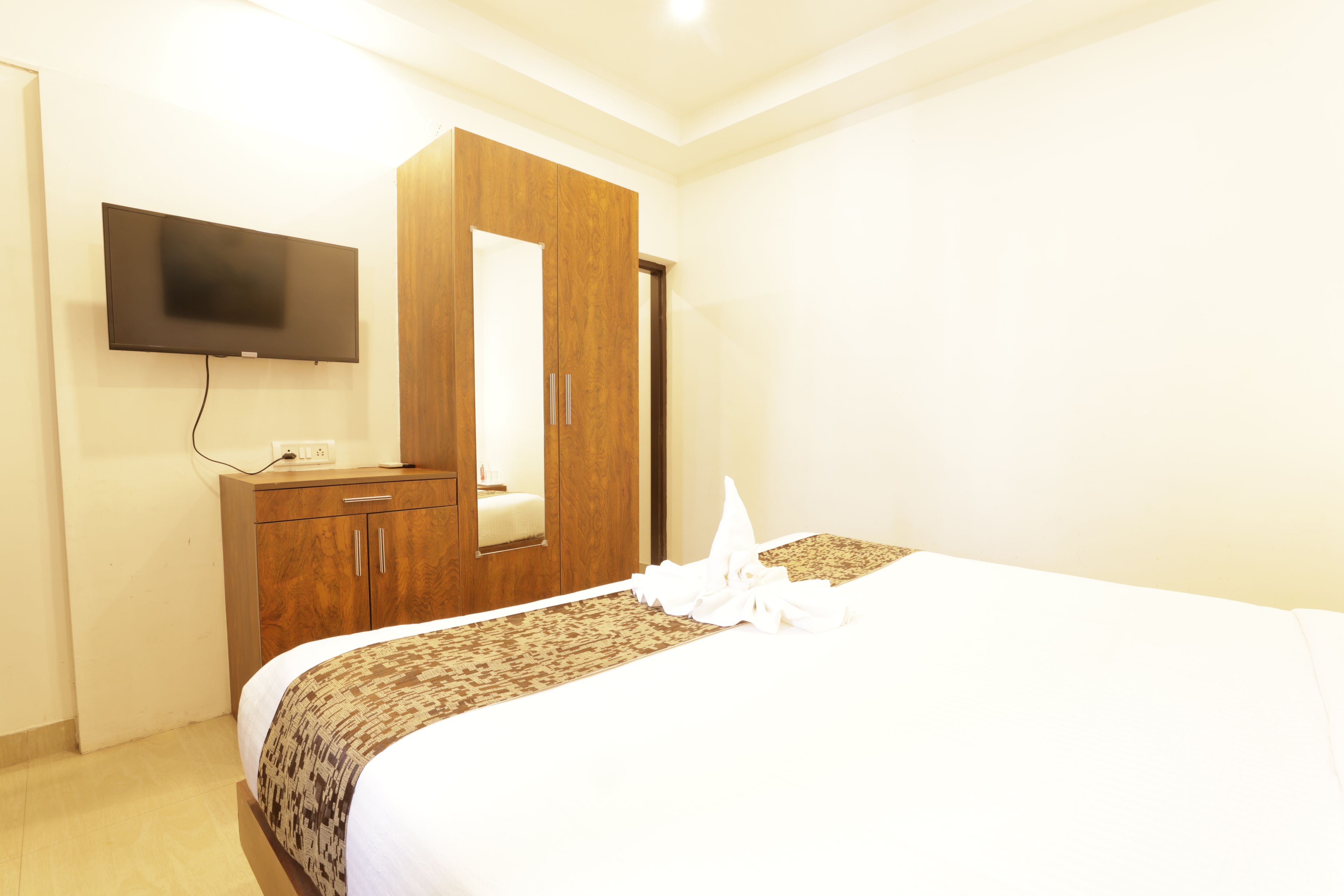 A hotel room with a bed, a wardrobe, a flat-screen TV, and a mirror.