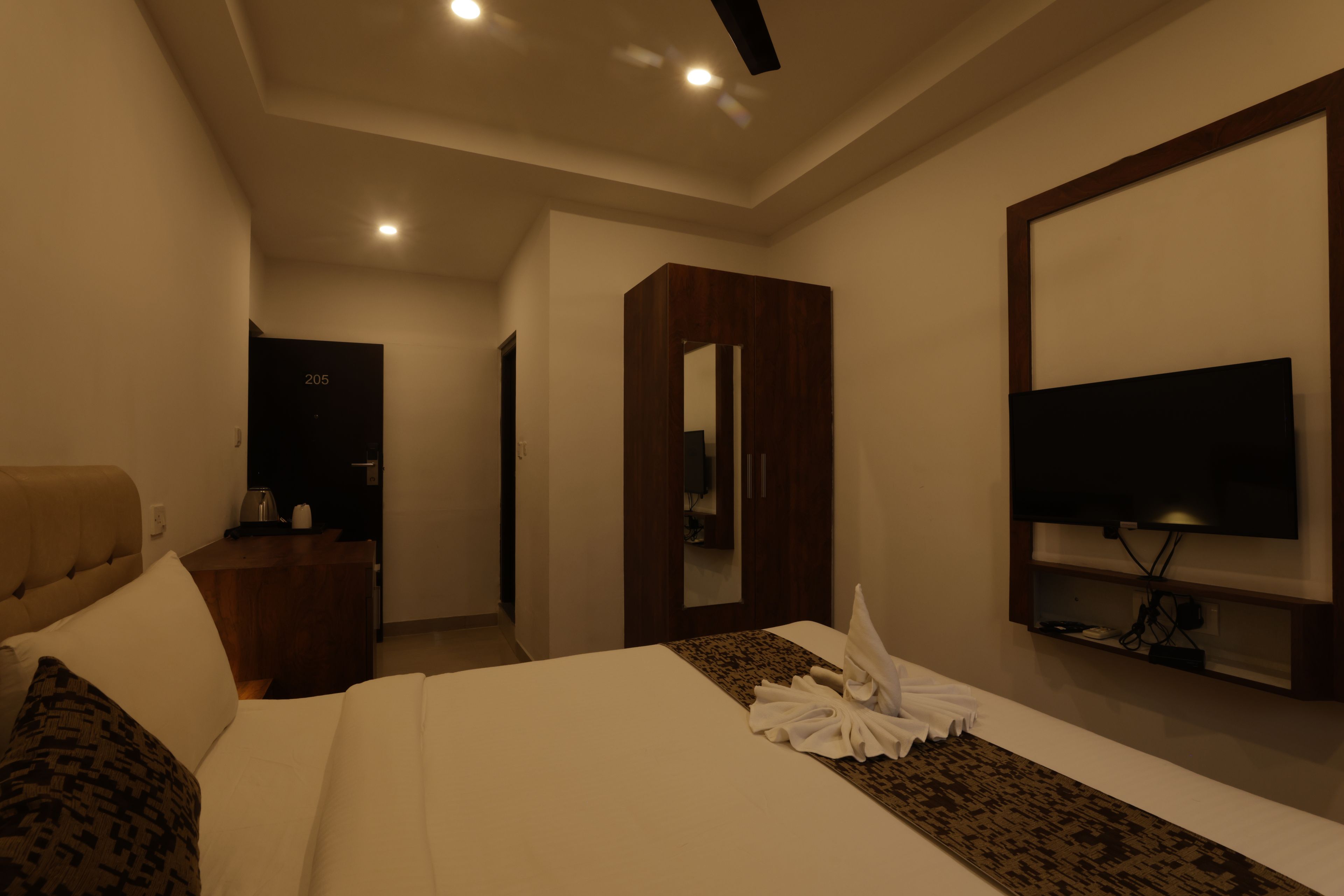 Habitación de hotel con cama, televisor, armario y escritorio con hervidor.