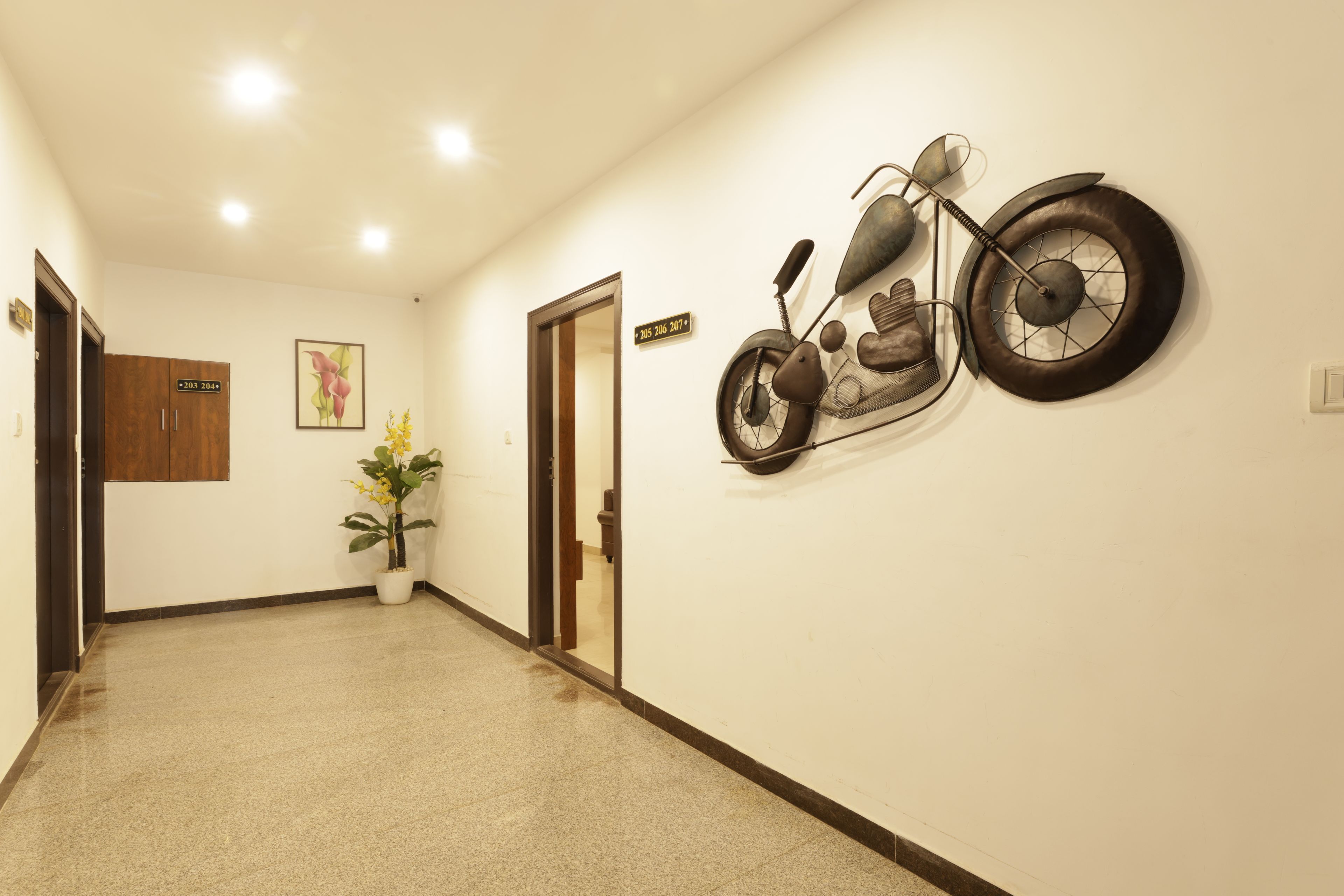 A hallway with a wall-mounted motorcycle decoration, a potted plant, and a door with a number sign.