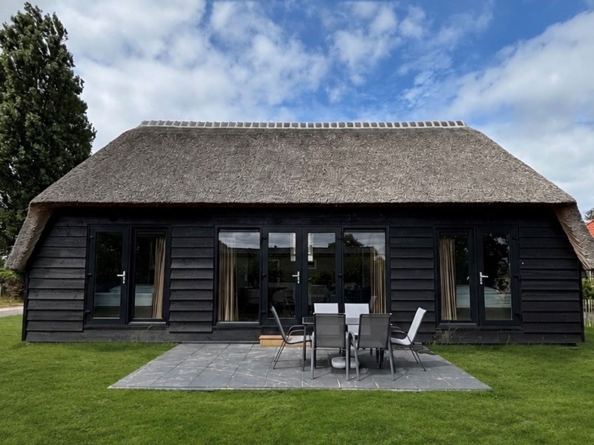 A modern building with a thatched roof, large windows, and a patio with outdoor furniture.