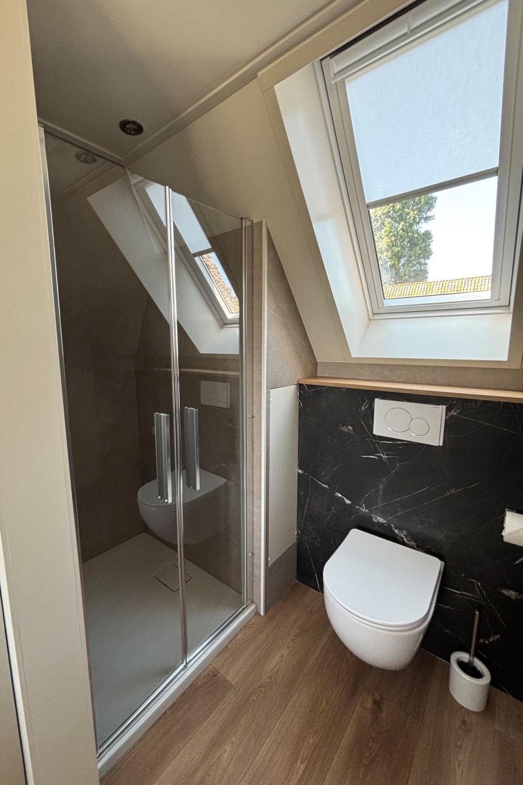 A modern bathroom with a skylight, a glass shower enclosure, and a marble backsplash.