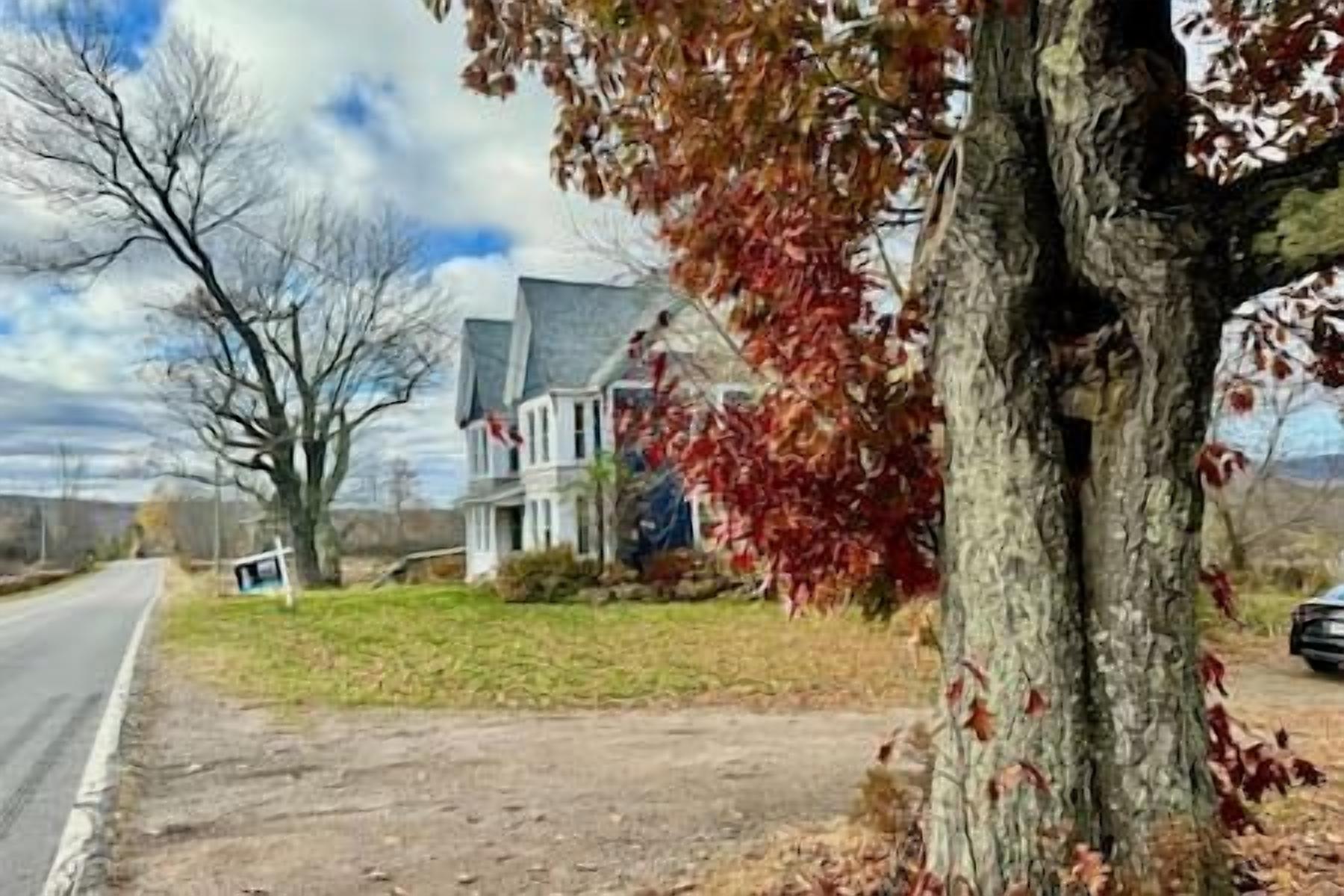A two-story house with a front yard, a driveway, and a tree with autumn leaves.