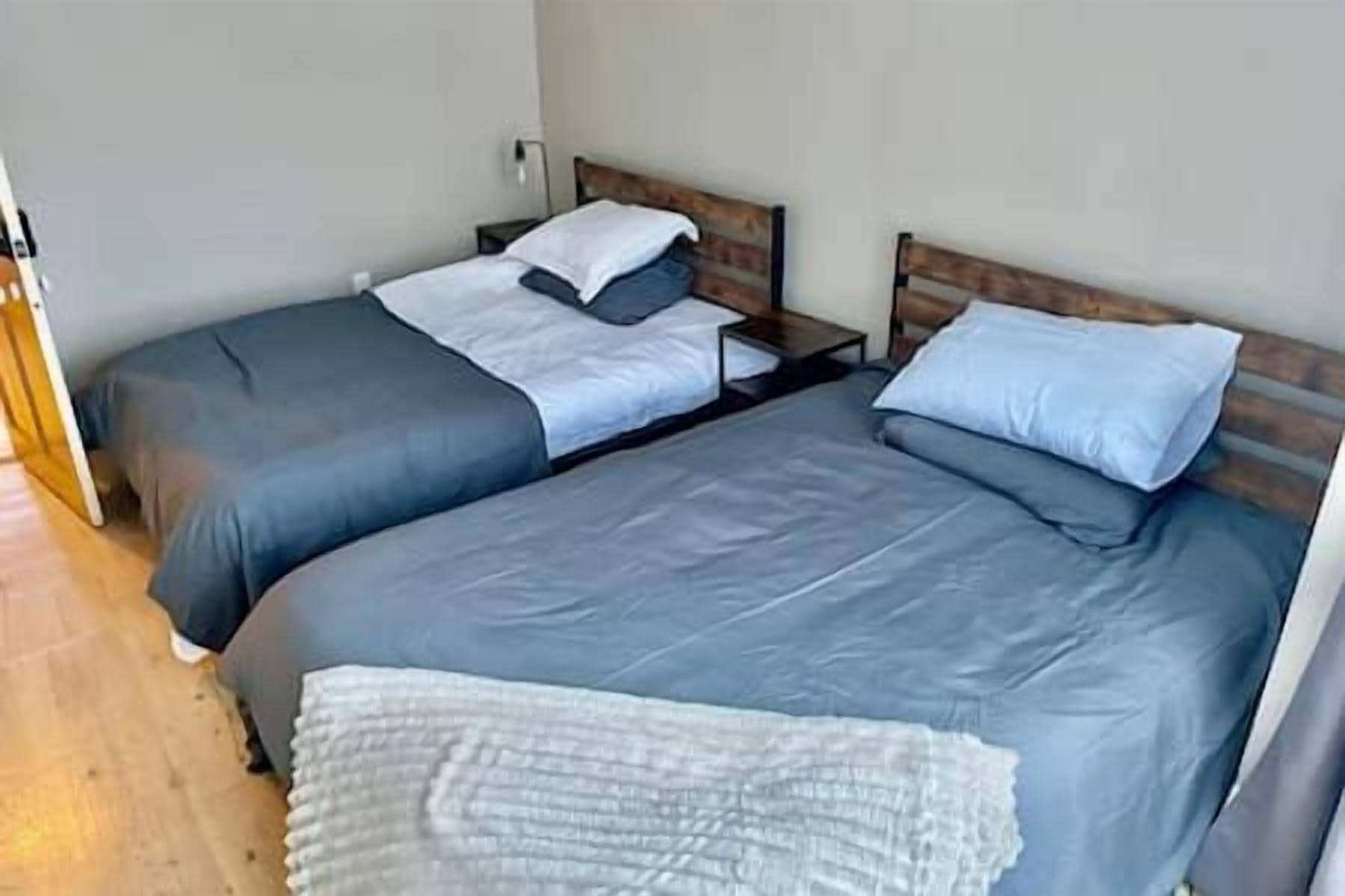 Une chambre avec deux lits, chacun doté d’une tête de lit en bois, et une couverture blanche posée sur le sol.