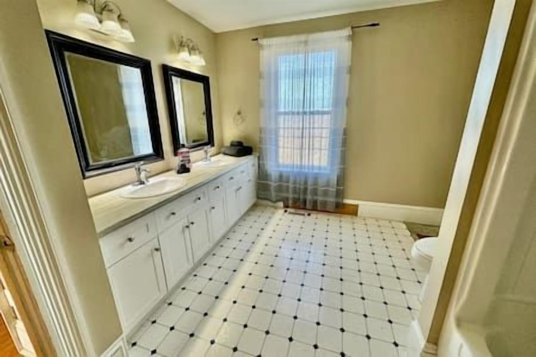Une salle de bain avec un sol carrelé, des toilettes, un lavabo avec un miroir et un rideau de douche.