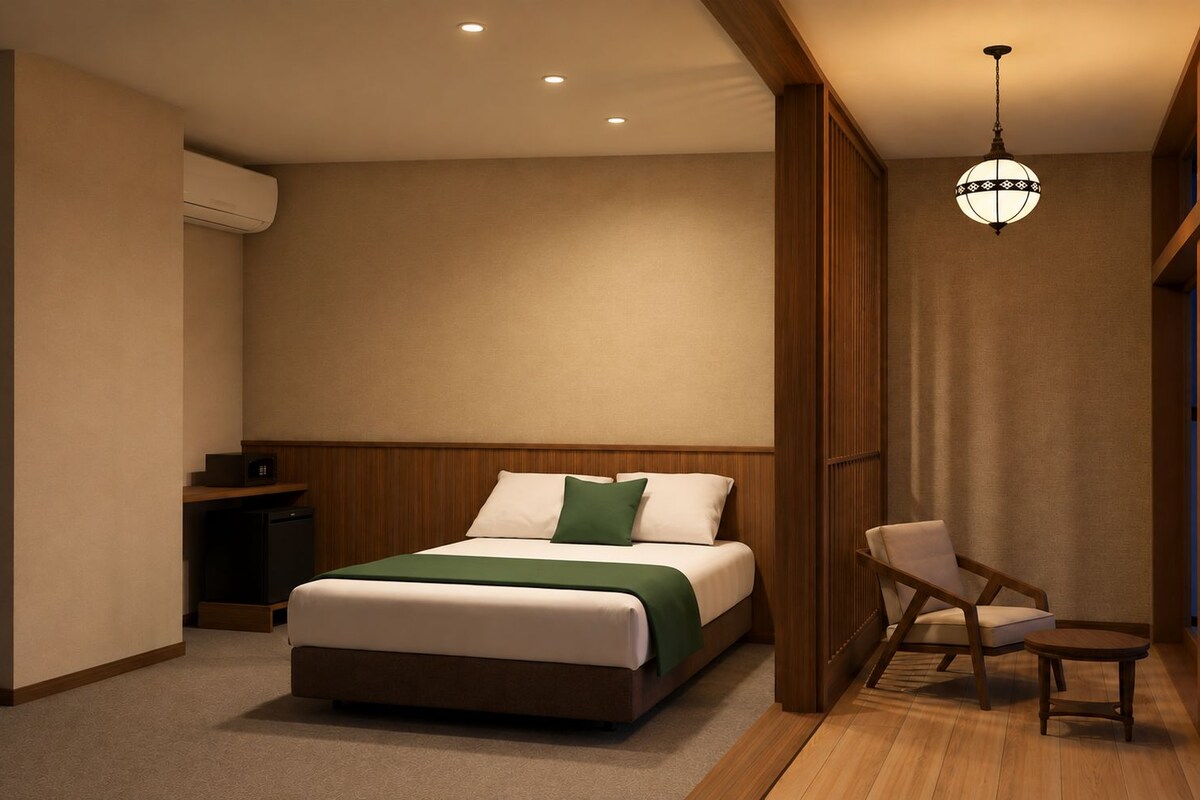 A hotel room with a bed, bedside table, chair, and a hanging light fixture.