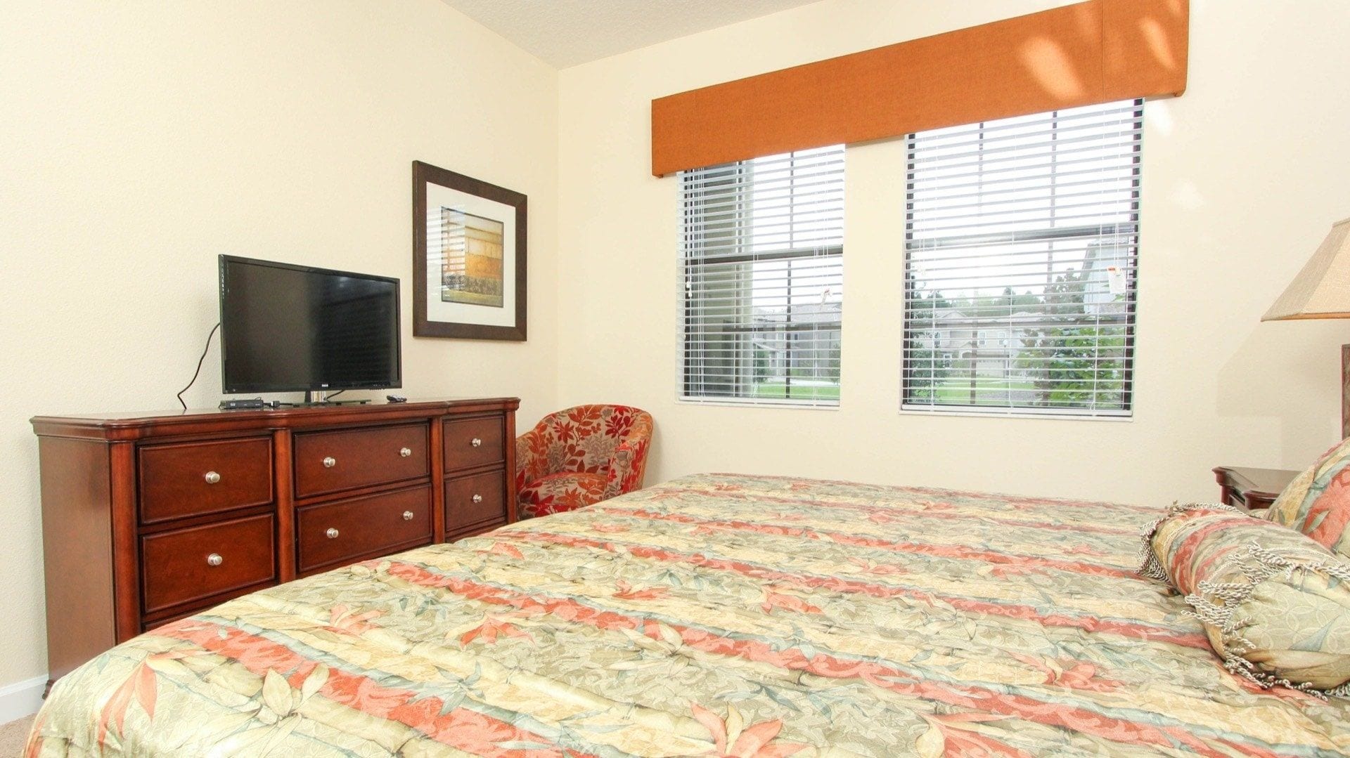 A bedroom with a bed, a dresser, a television, and two windows with blinds.