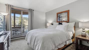 Un dormitorio con una cama grande, un escritorio, una silla y un balcón con vistas a árboles y colinas.