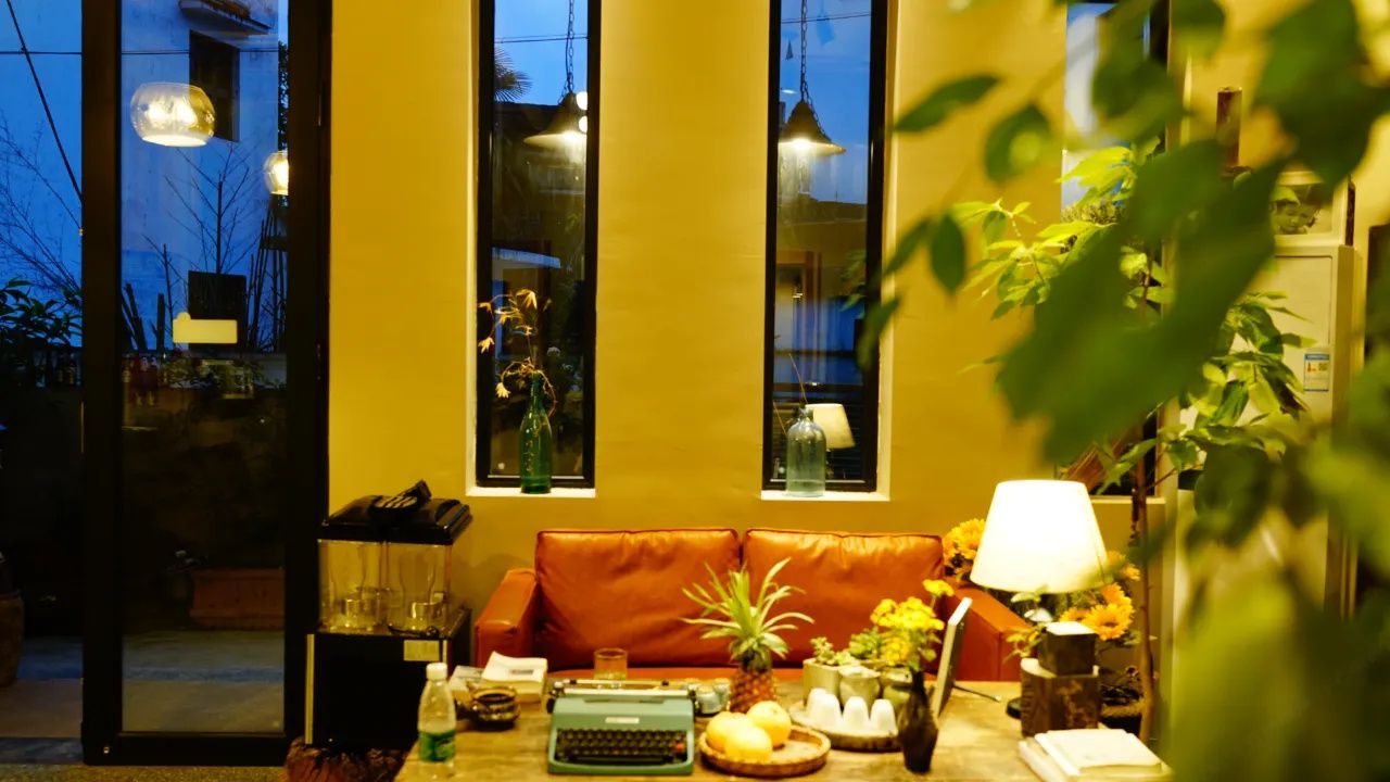 Ein gemütliches Zimmer mit einer Couch, einem Tisch mit einer Schreibmaschine, einer Lampe und einem Fenster mit Blick nach draußen.