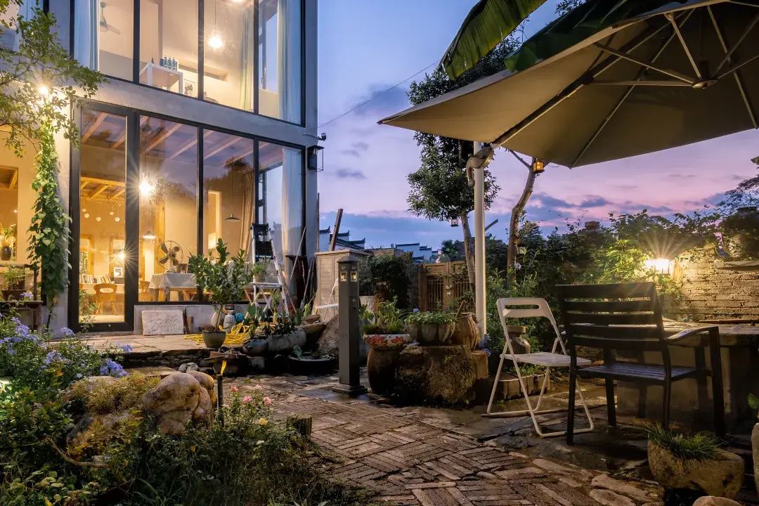 Un patio al aire libre con una mesa y sillas para comer, rodeado de macetas con plantas y un sendero de piedra.