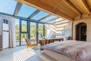 A bedroom with a large bed, a wooden chair, a small table, and a view of the outdoors through large windows. - Wuyuan Jianwai Rill Wild Homestay (Shangrao)