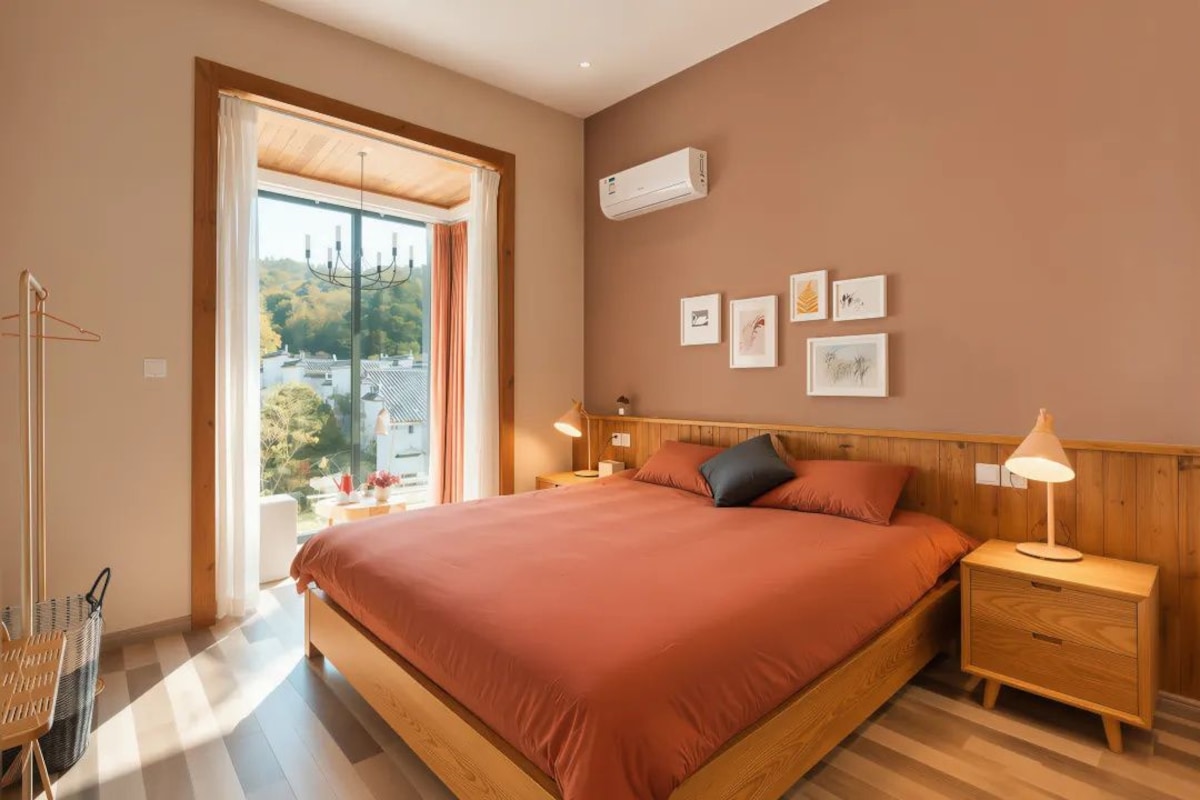 A bedroom with a large bed, a nightstand, a lamp, a wall-mounted air conditioner, and framed pictures.