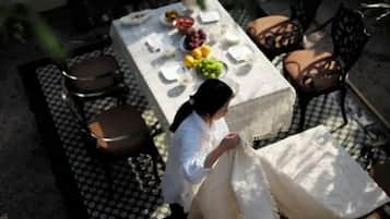 A person seated at an outdoor table with a white tablecloth, surrounded by chairs and a dining set.