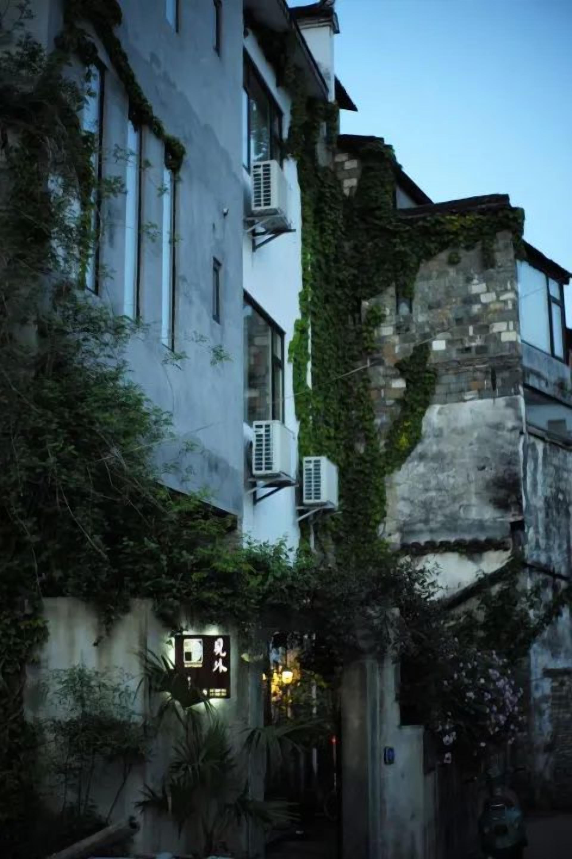 Uma viela estreita com edifícios de ambos os lados, alguns com hera e um aparelho de ar condicionado à vista.