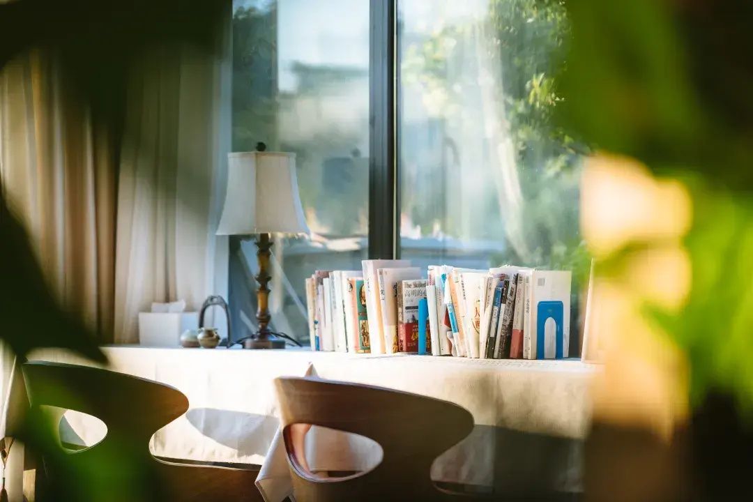 Una habitación con ventana, una lámpara y una mesa con revistas.