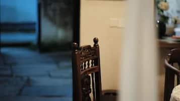 Una habitación con piso estampado, una silla de madera, una mesa con un jarrón y una ventana con vista al exterior.