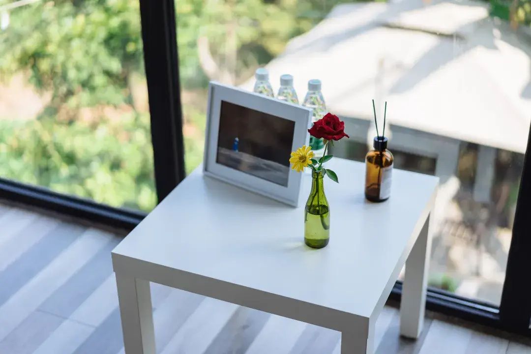 Una mesa blanca con un marco de fotos, un jarrón con flores y una botella de agua.