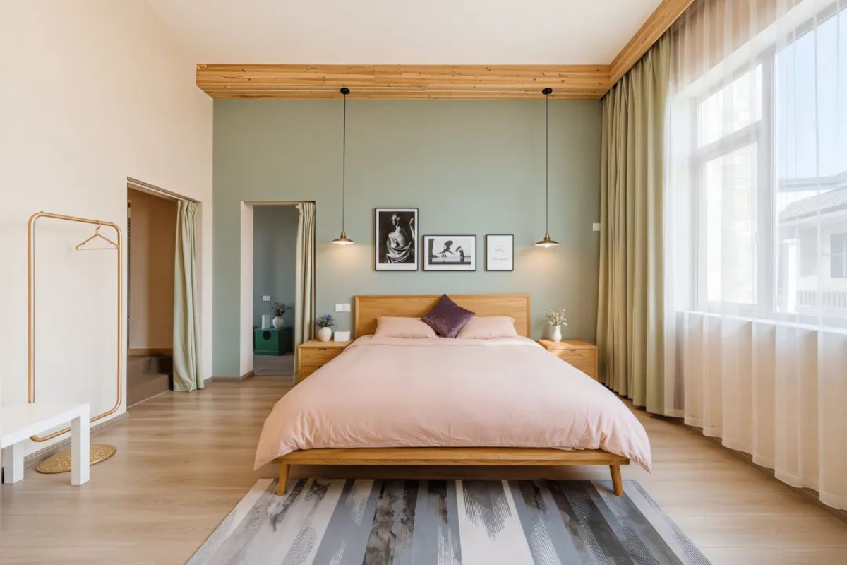 A bedroom with a bed, bedside tables, a hanging light fixture, and a window with curtains.