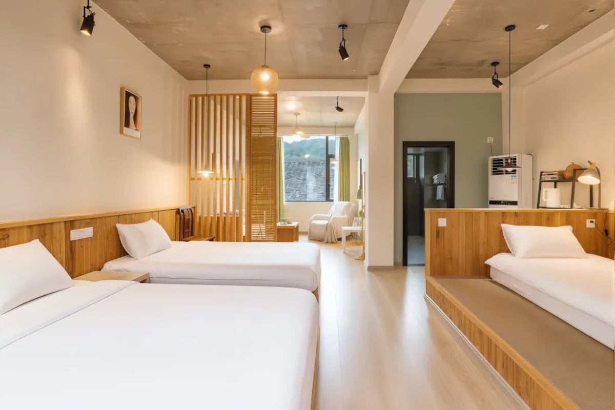 A hotel room with two beds, a wooden headboard, a large window, and a view of the outdoors.