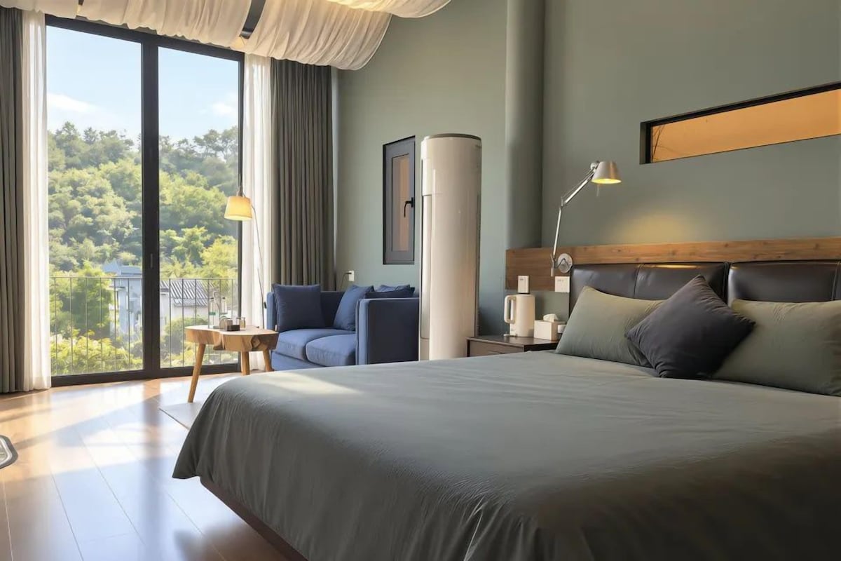 A hotel room with a large bed, a seating area, a view through the window, and a modern design.