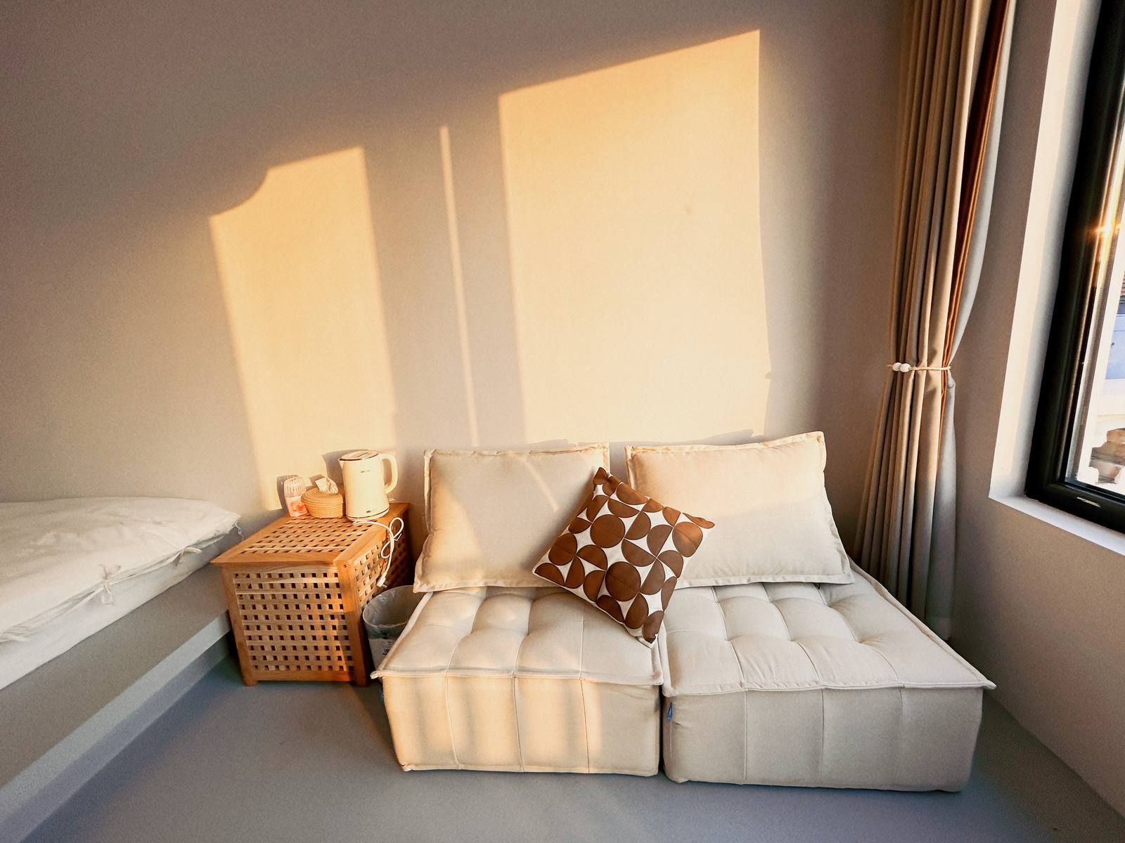 Una habitación acogedora con sofá cama, una mesita de madera con tetera y juego de té, y una ventana con cortinas.