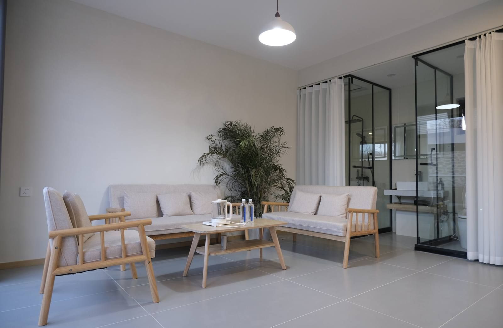 En moderne stue med sofa, to lænestole, et sofabord og en stor potteplante.