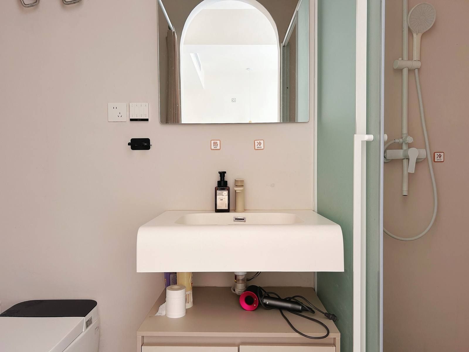 Een badkamer met een witte wastafel, een spiegel erboven, een handdouche en een haardroger op het aanrecht.