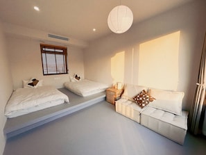 A bedroom with two beds, a sofa, a hanging light fixture, and a window with blinds.