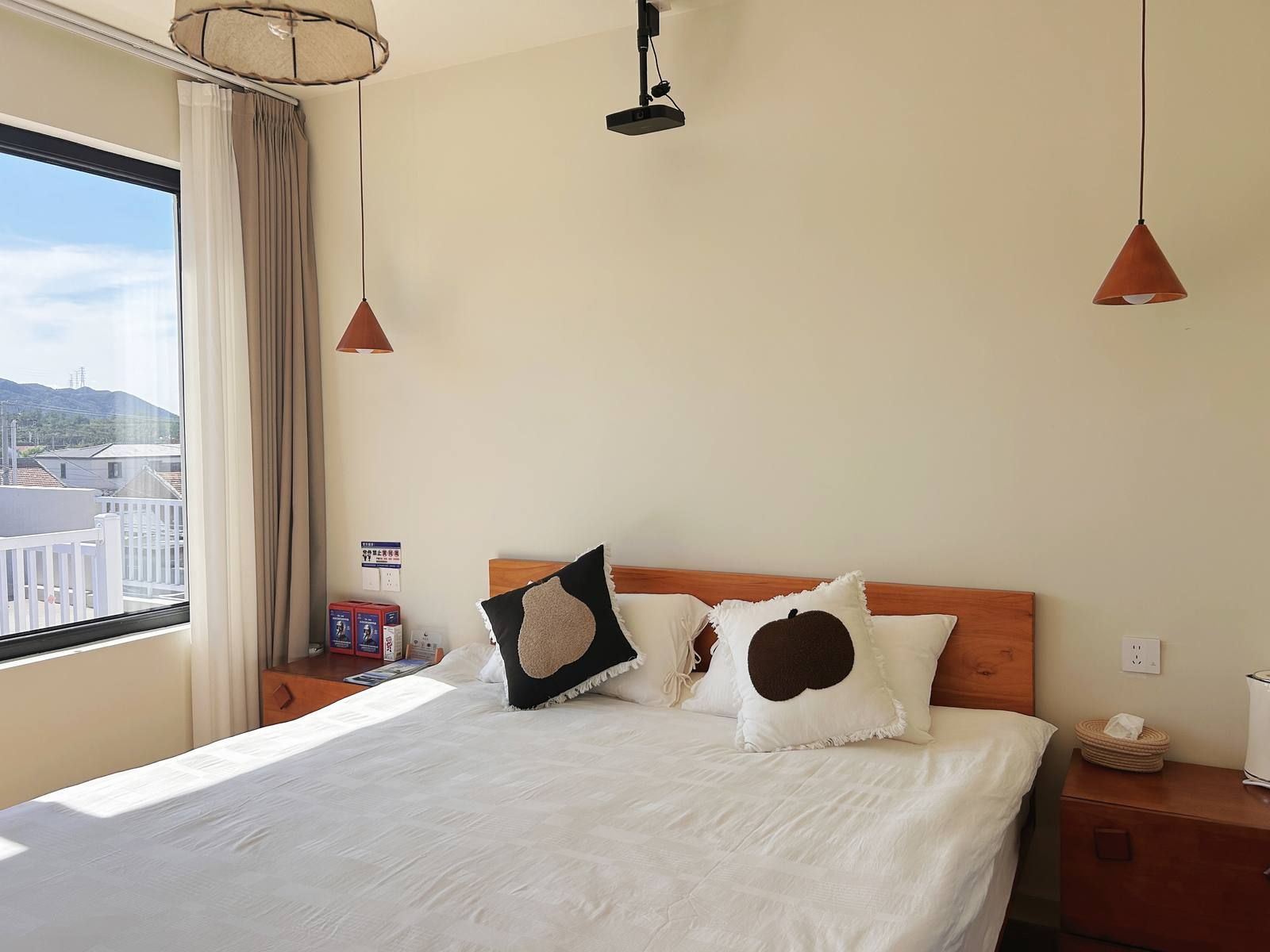Ein Hotelzimmer mit einem Bett, zwei Nachttischen, einem Fenster mit Vorhängen und Blick auf Gebäude.