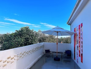 A balcony with a table and chairs, a large umbrella, and a wall with vertical banners.