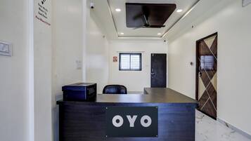 A reception desk with a sign reading 'OYO' in a hallway with a ceiling fan, a window, and a door.