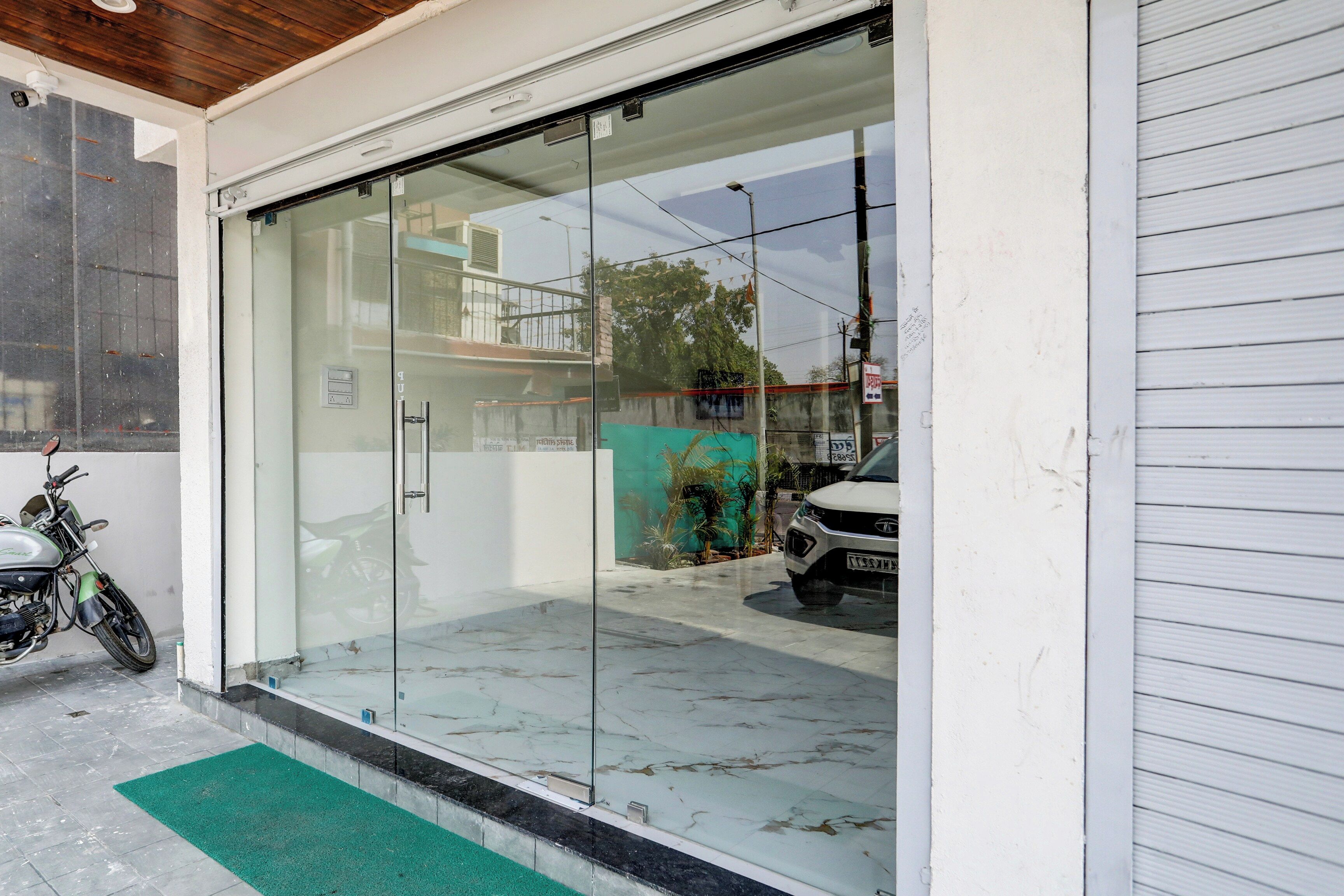 L'ingresso di un edificio con una porta in vetro, una motocicletta parcheggiata all'esterno e un tappetino verde a terra.