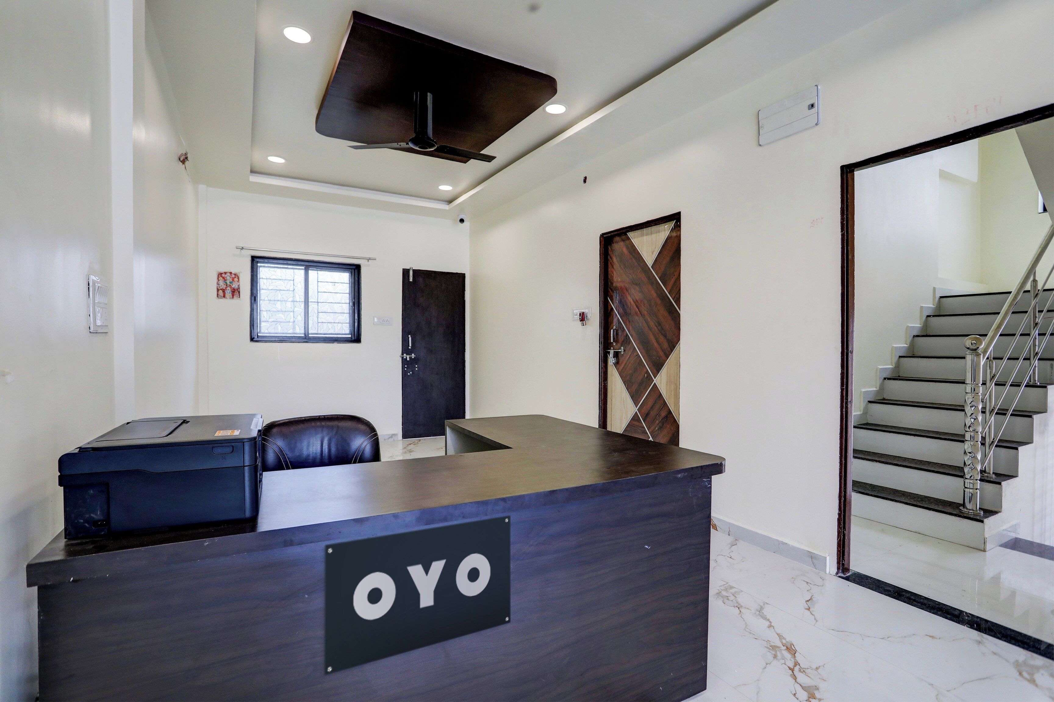 A reception desk with a sign reading 'OYO' in a modern office space with a staircase and a window.