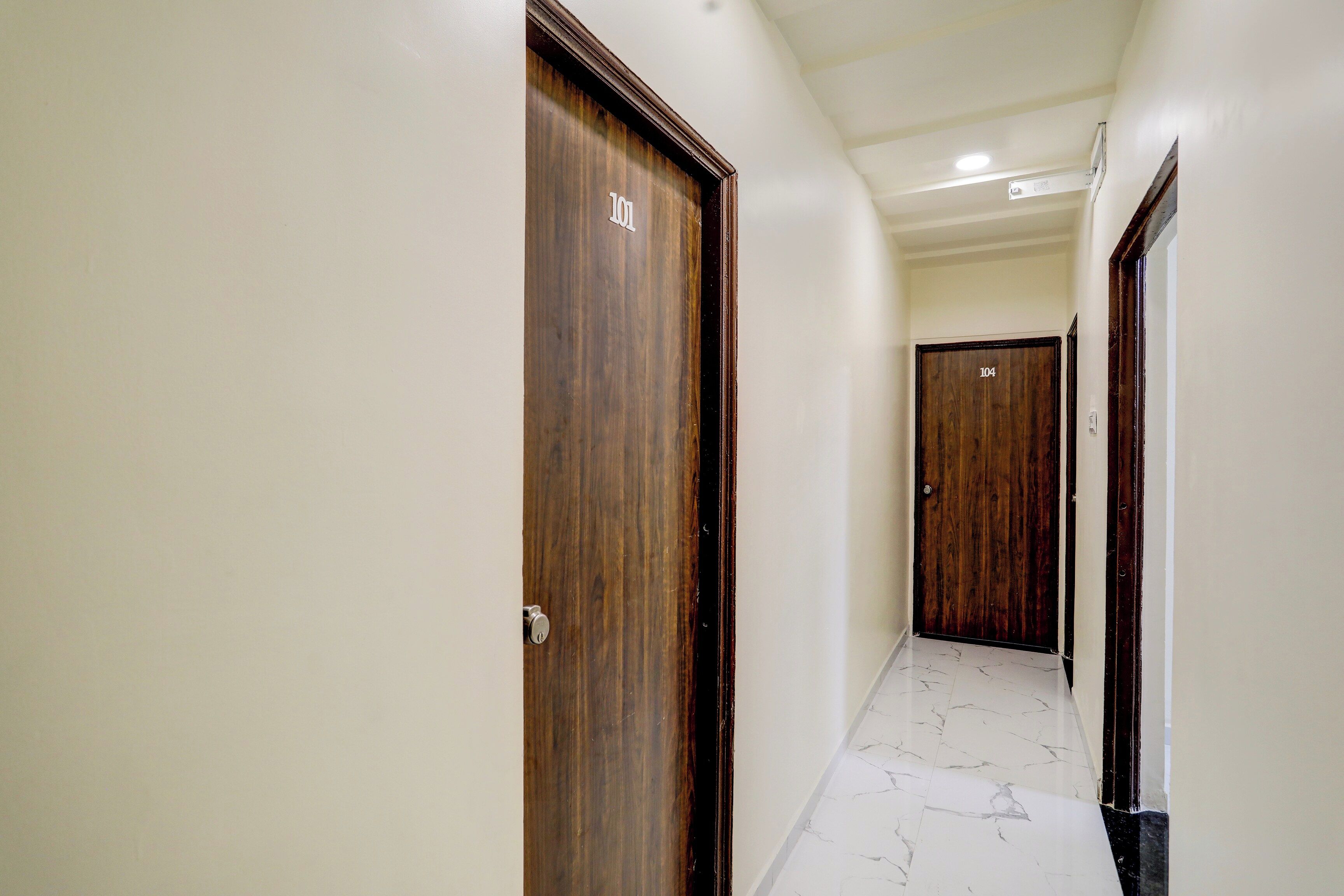 Corredor com portas de madeira, numeradas 101 e 104, e piso de mármore.