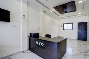 Un mostrador de recepción con un letrero que dice 'OYO' en el vestíbulo de un hotel, con un ventilador de techo, una ventana y una puerta.