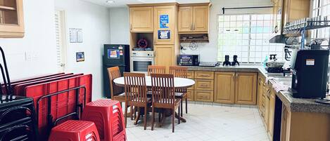 A kitchen with wooden cabinets, a dining table with chairs, a refrigerator, an oven, and a coffee machine.