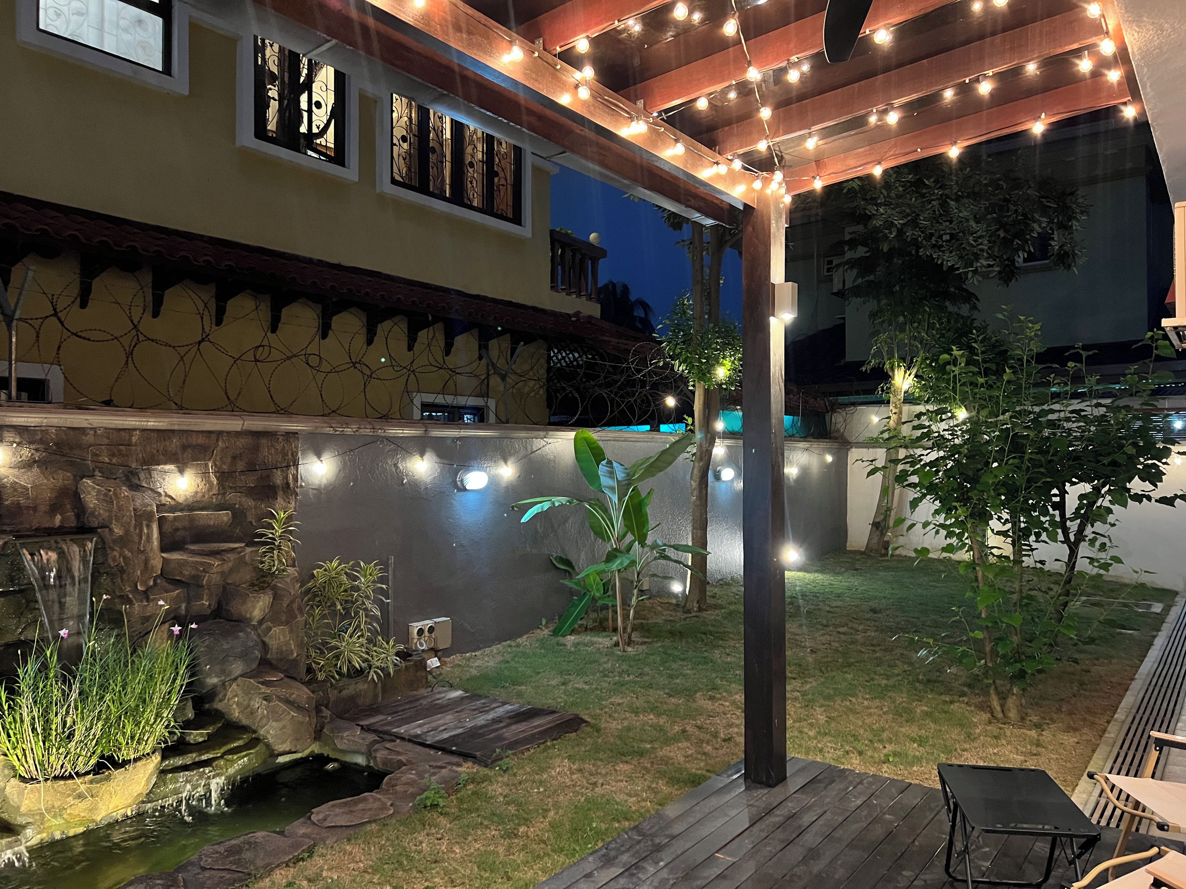 Un patio con pared de piedra, un pequeño elemento acuático y luces colgantes.