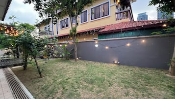 A residential building with a red-tiled roof, a balcony with a railing, and a garden area with grass and trees.