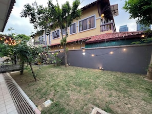 A residential building with a red-tiled roof, a balcony with a railing, and a garden area with grass and trees.