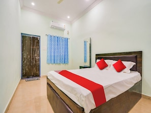 A hotel room with a bed, a nightstand, a mirror, a window with curtains, and an air conditioning unit. - Hotel O Kanha (Nagpur)