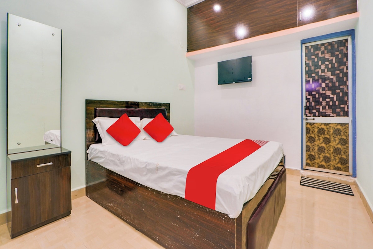 A bedroom with a bed, a nightstand, a mirror, a wall-mounted TV, and a patterned door.